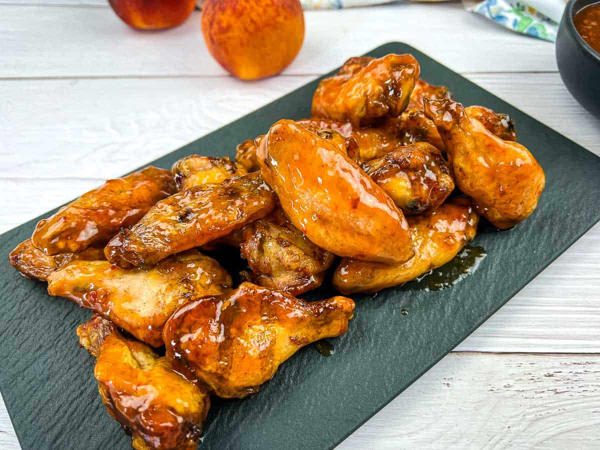 Smoked and glazed peach-chipotle chicken wings on a black plate.