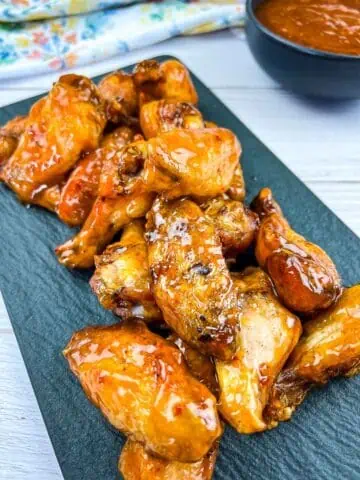Chicken wings on a plate with sauce on the side.