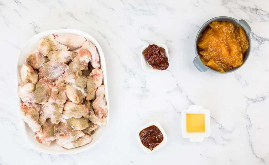 A plate of chicken wings and sauce on a marble table.