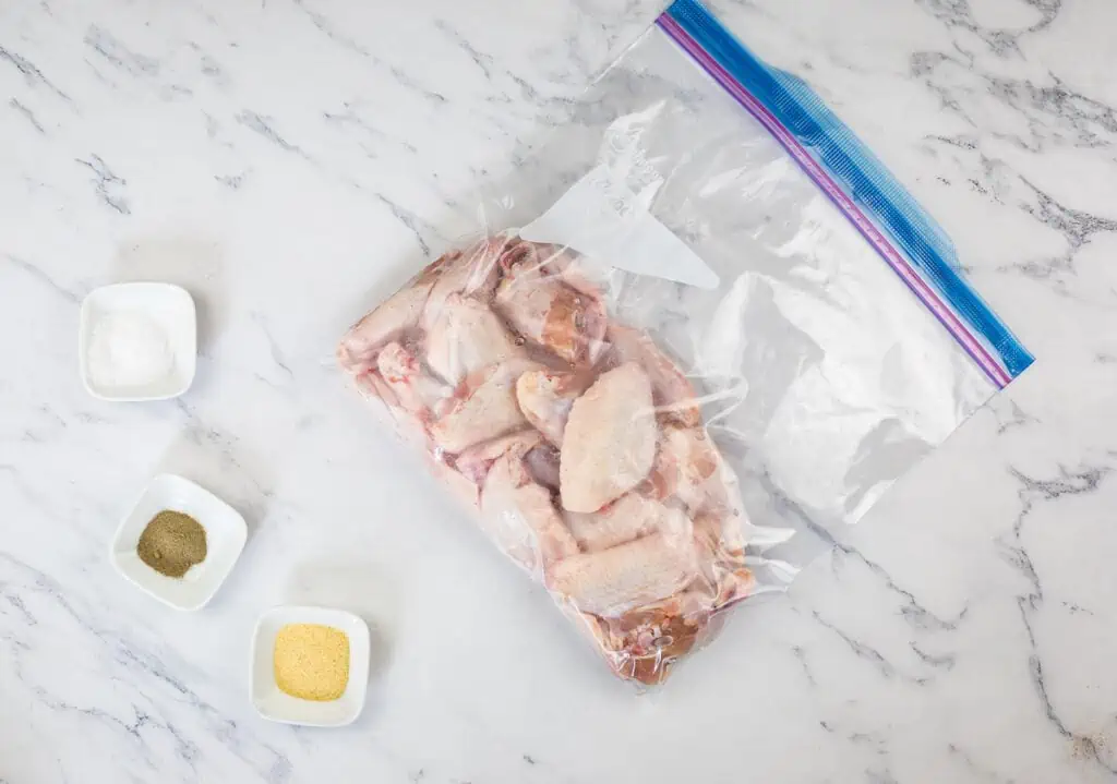 Chicken wings in a plastic bag on a marble countertop.