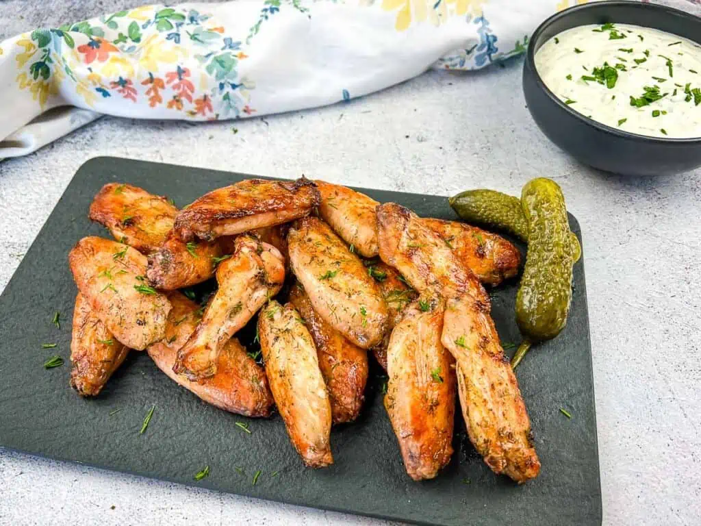 Chicken wings on a plate with pickles and dipping sauce.