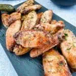 Grilled chicken wings on a plate with pickles and dip.