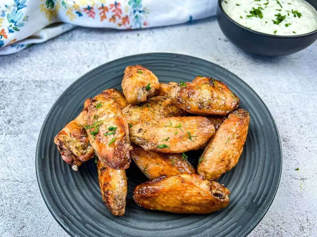 Chicken wings on a black plate with dipping sauce.