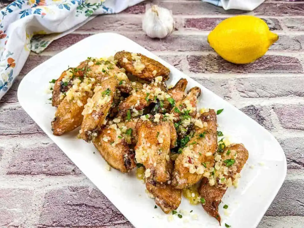 Chicken wings with lemon and garlic on a white plate.