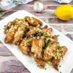 Chicken wings with lemon and garlic on a white plate.