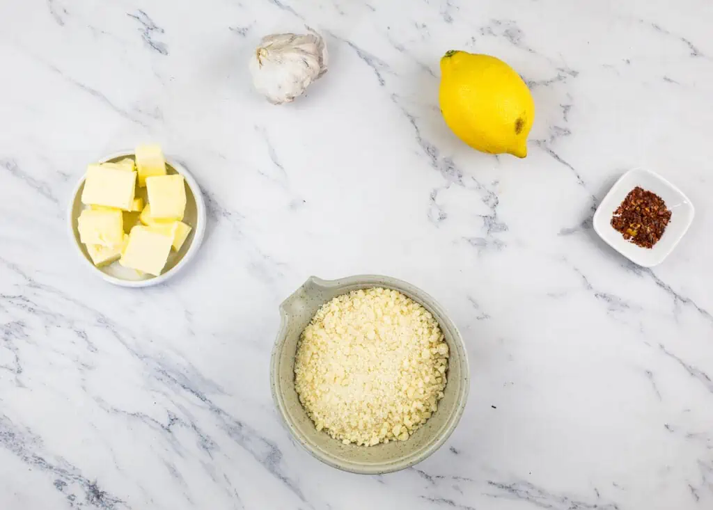 Bowls of parmesan, butter, garlic and lemon on a marble table.