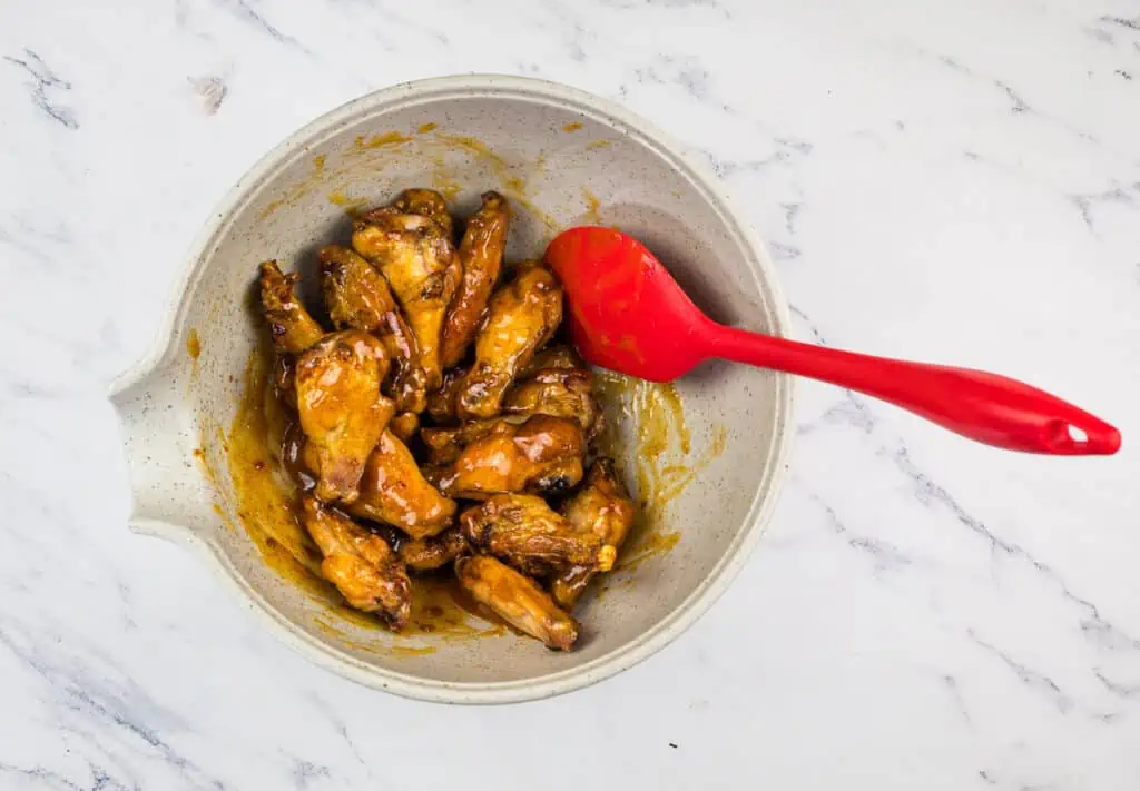 Chicken wings in a bowl with a red spoon.