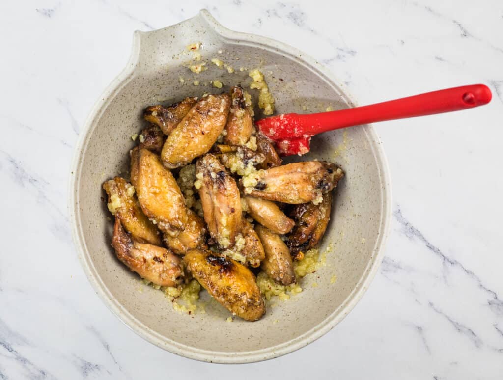 Chicken wings in a bowl with a red spoon.