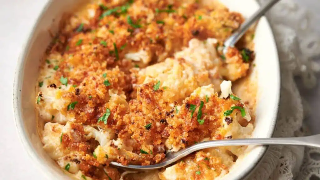 Cheesy cauliflower casserole in a white dish with spoons.