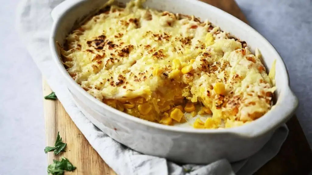 Cheesy corn casserole on a wooden cutting board.