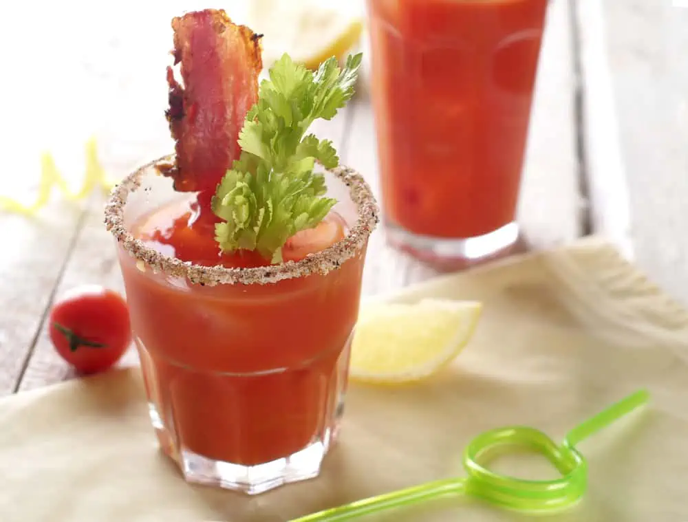Two glasses of bloody mary with bacon garnish.
