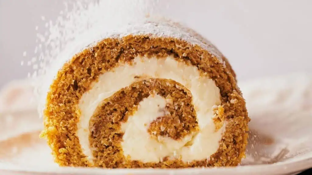 A slice of pumpkin roll being sprinkled with powdered sugar.