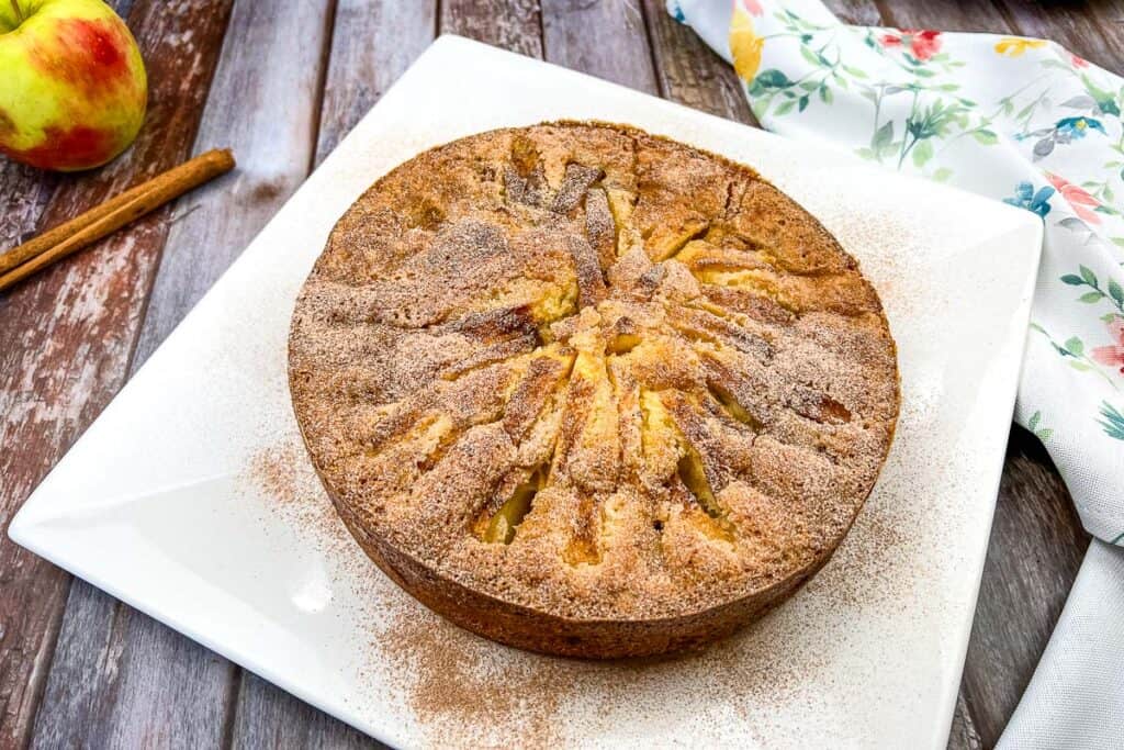 An apple cake on a white plate with cinnamon sticks.