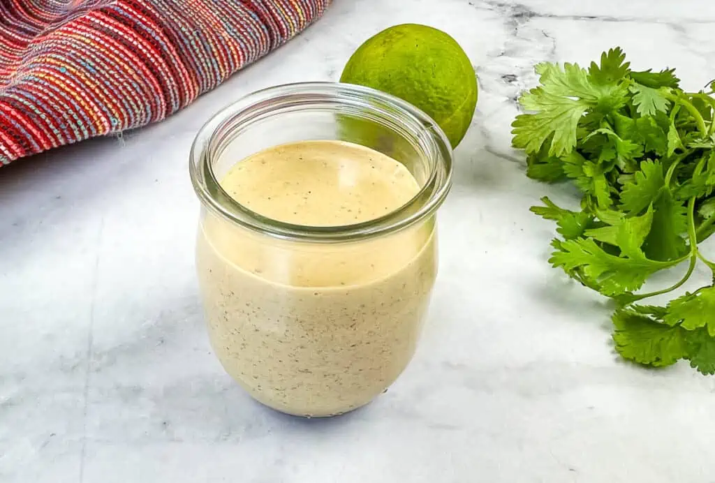 A jar with burrito sauce in it with lime and garlic in the background.