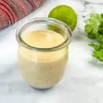 A jar with Burrito Sauce in it with lime and garlic in the background.