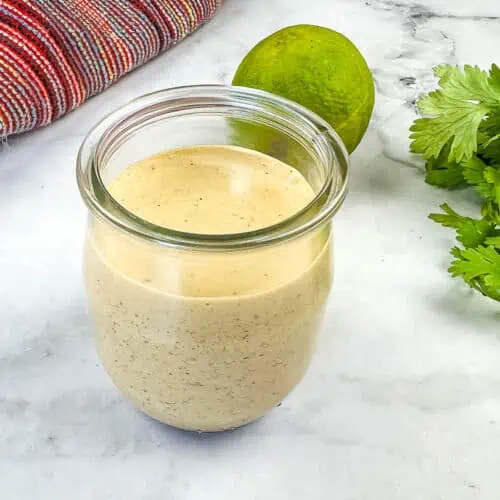 A jar with Burrito Sauce in it with lime and garlic in the background.
