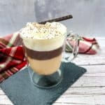 A cup of coffee in a glass with whipped cream and a cinnamon stick.