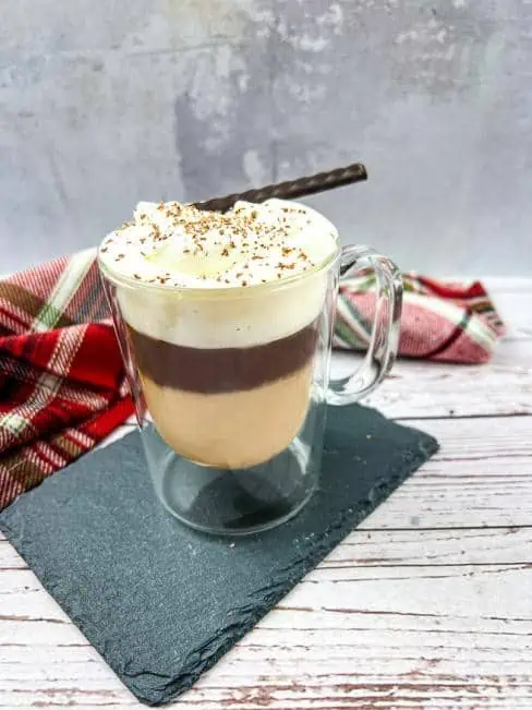 A cup of coffee in a glass with whipped cream and a cinnamon stick.