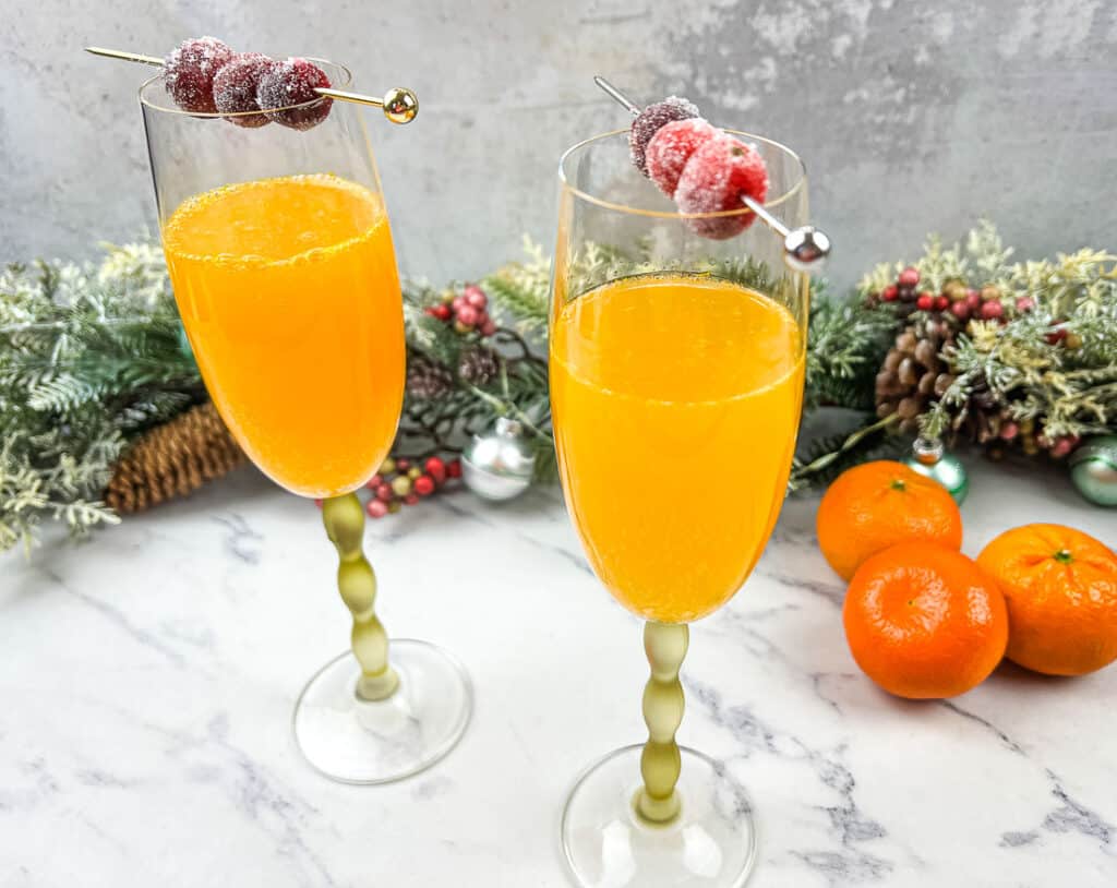 Two glasses of Christmas Mimosas with oranges and cranberries.