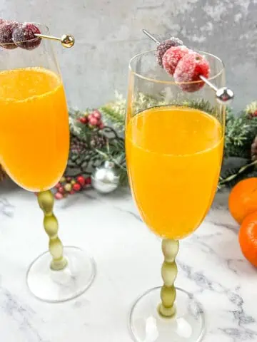 Two glasses of Christmas Mimosas with oranges and cranberries.