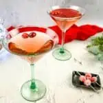 Two martinis with cranberries and decorations on a table.