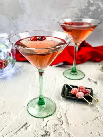 Two martinis with cranberries and decorations on a table.