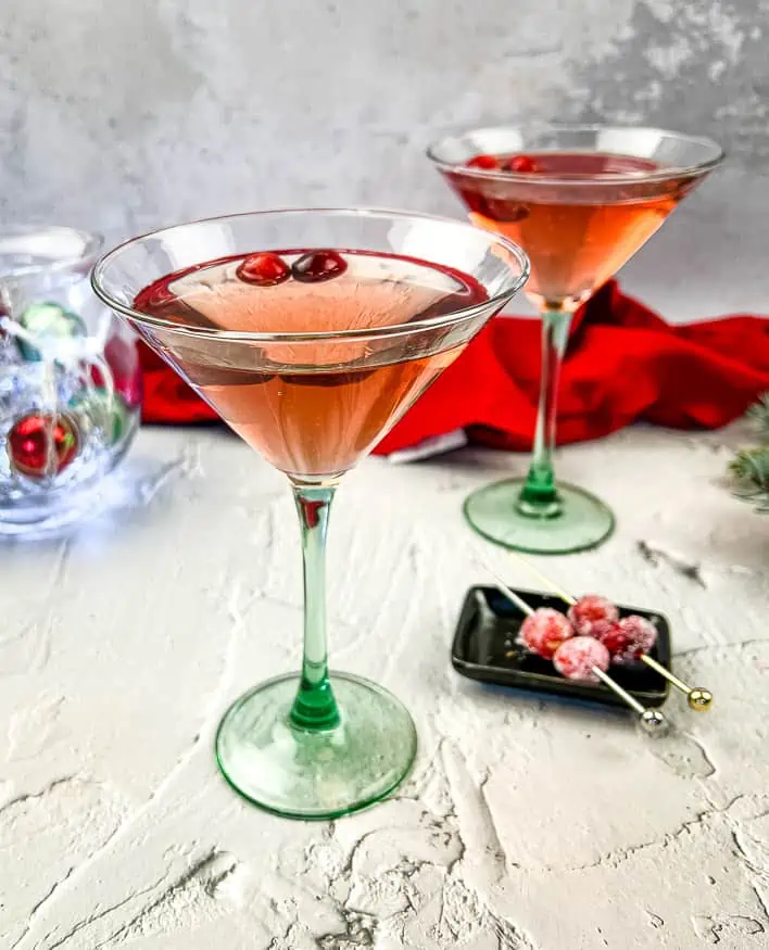 Two martinis with cranberries and decorations on a table.