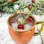 A copper moscow mule with cranberries and a sprig of rosemary.