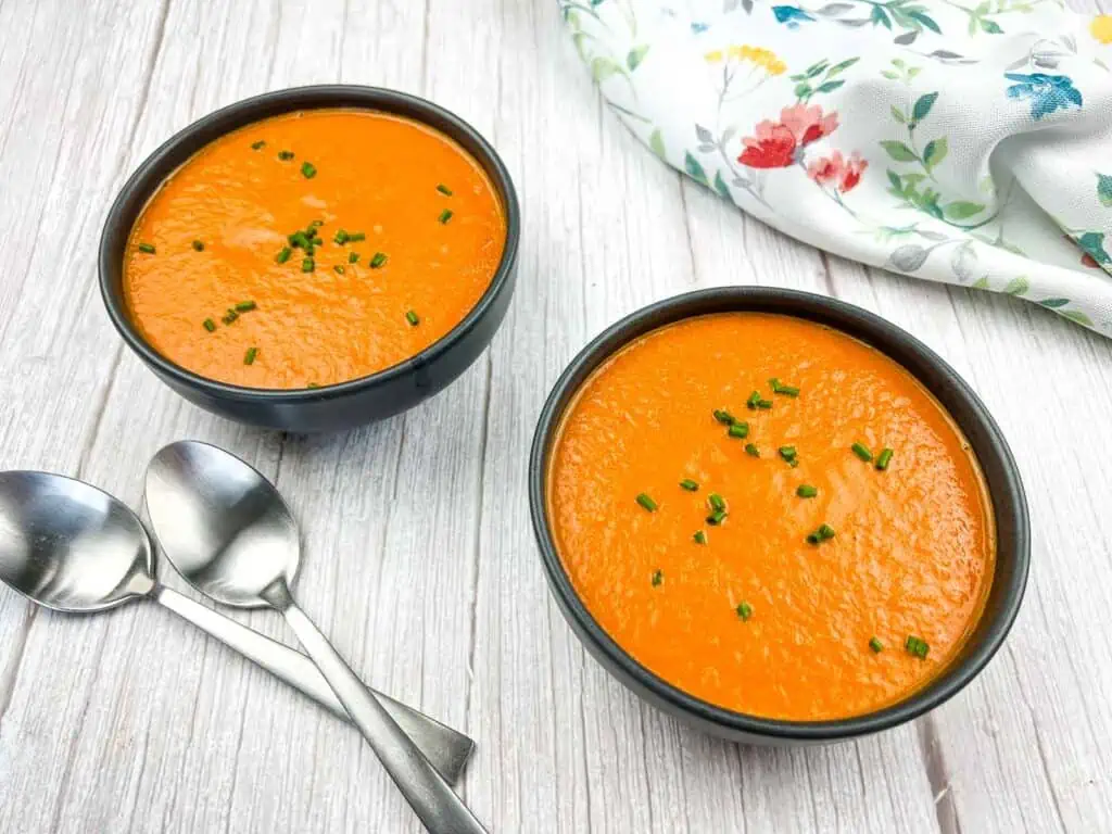 Two bowls of carrot soup with spoons on a wooden table.