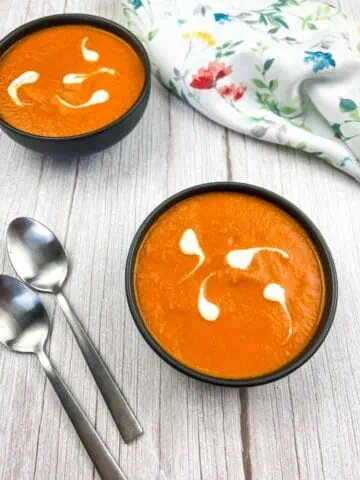 Two bowls of carrot soup on a wooden table.