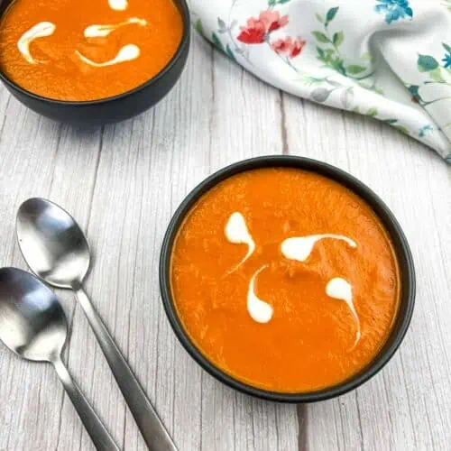 Two bowls of carrot soup on a wooden table.