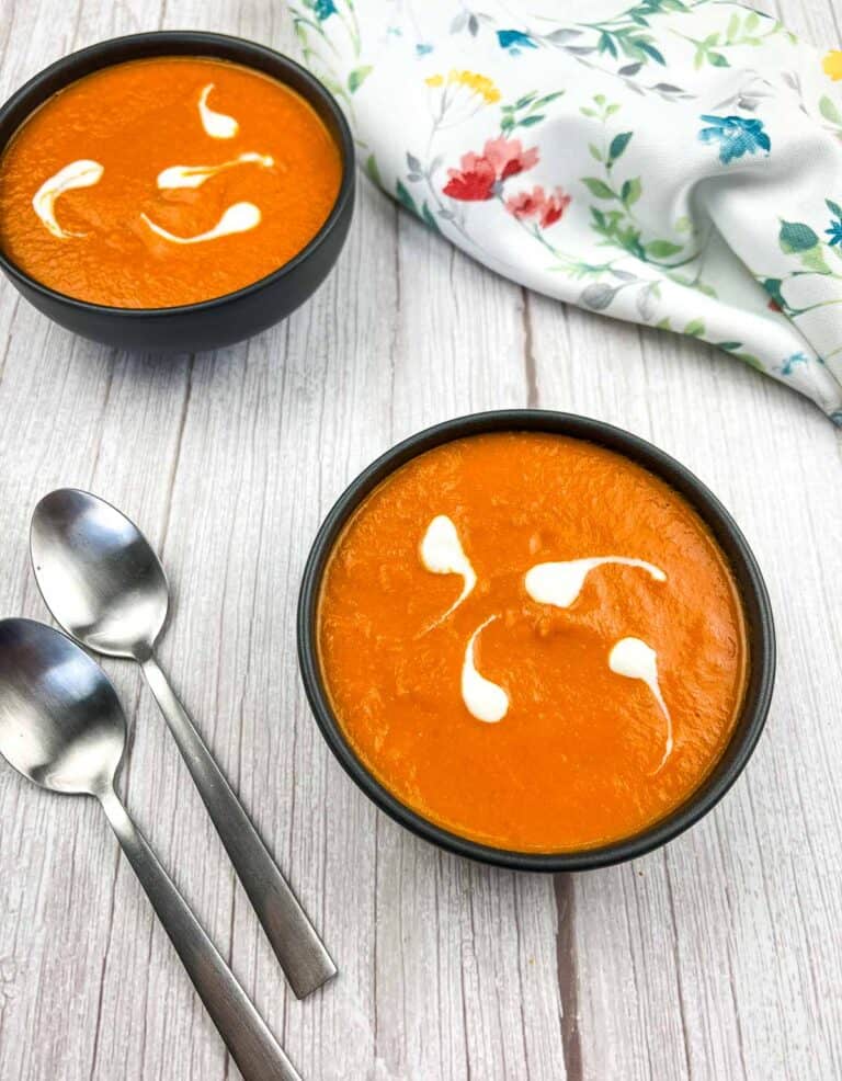 Two bowls of carrot soup on a wooden table.