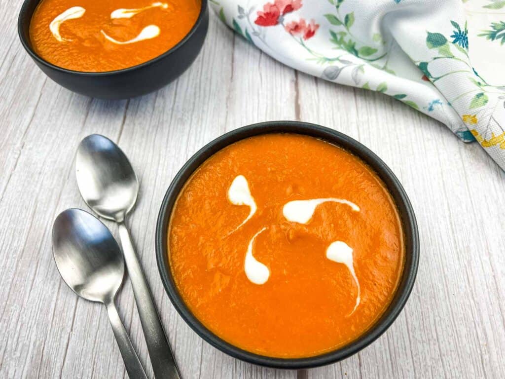 A bowl of Oven Roasted Tomato Soup with sour cream and spoons.