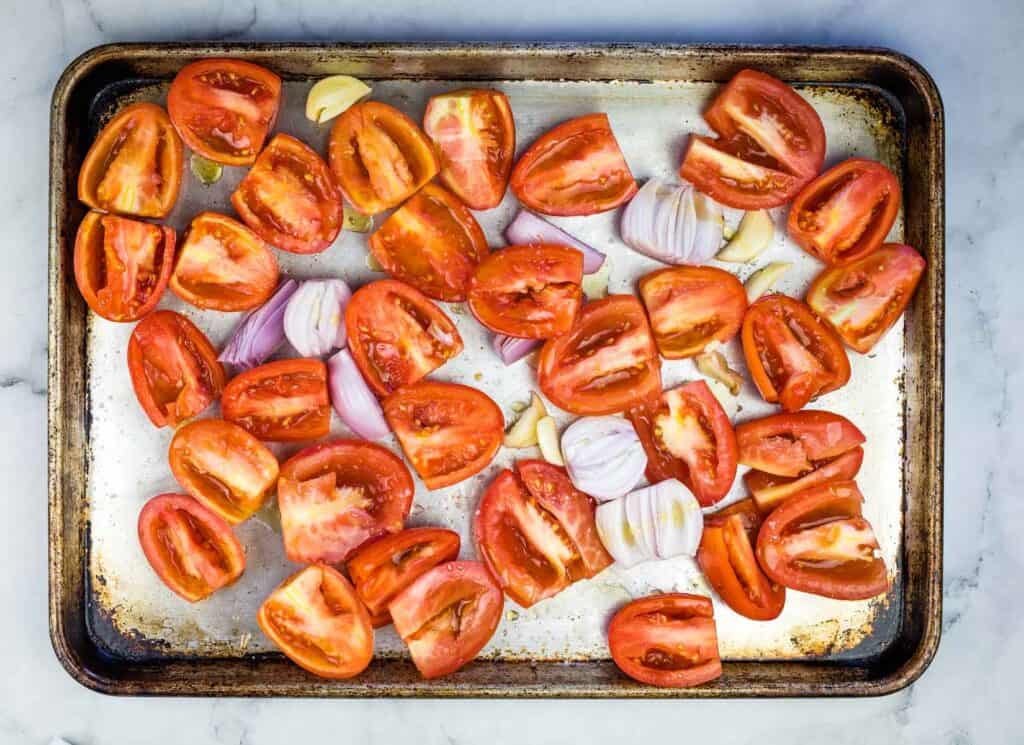 Sliced tomatoes and onions on a baking sheet.