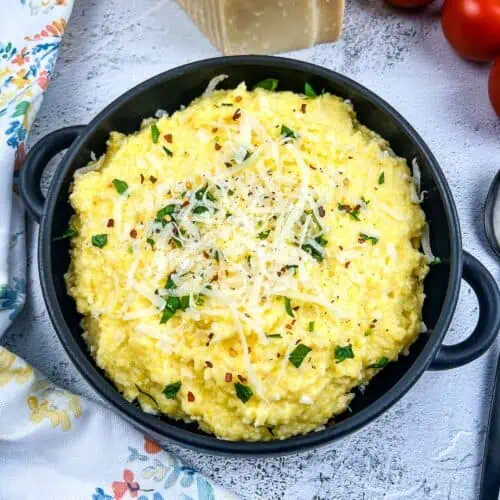 A bowl of polenta with mascarpone with tomatoes in the background.