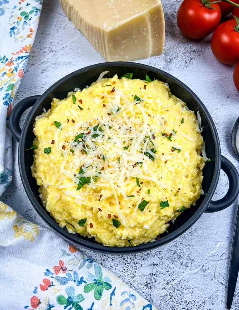 A bowl of polenta with mascarpone with tomatoes in the background.