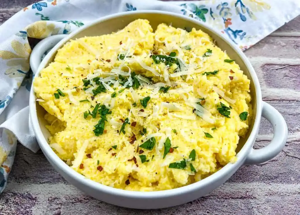 Polenta with mascarpone in a white bowl with parmesan cheese.