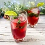 Two glasses of Pomegranate Mojitos with lime and mint.