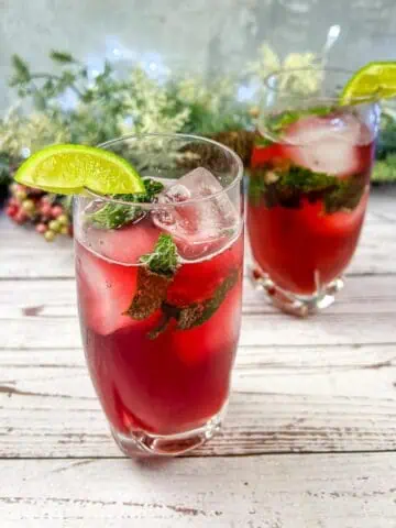 Two glasses of Pomegranate Mojitos with lime and mint.