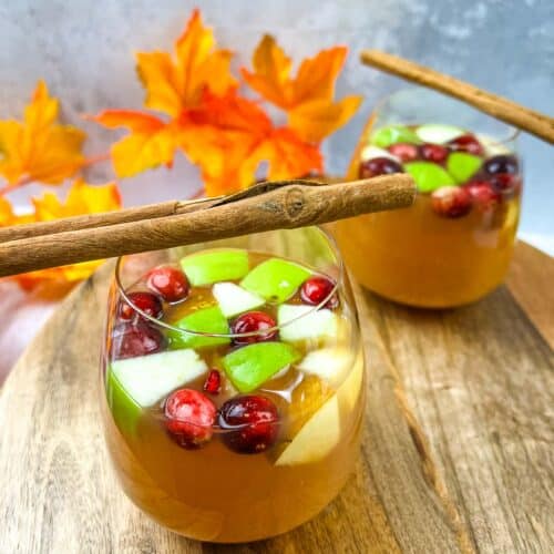 Two glasses of cranberry cranberry sangria with cinnamon sticks.