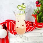 A drink with cranberries and a christmas tree on a table.