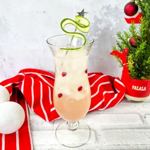 A drink with cranberries and a christmas tree on a table.