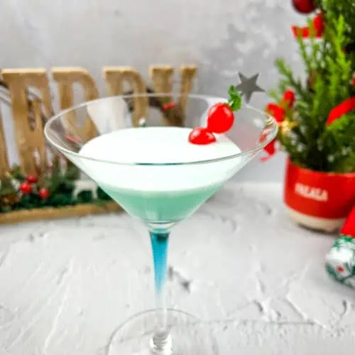 A martini in a glass with a christmas tree in the background.