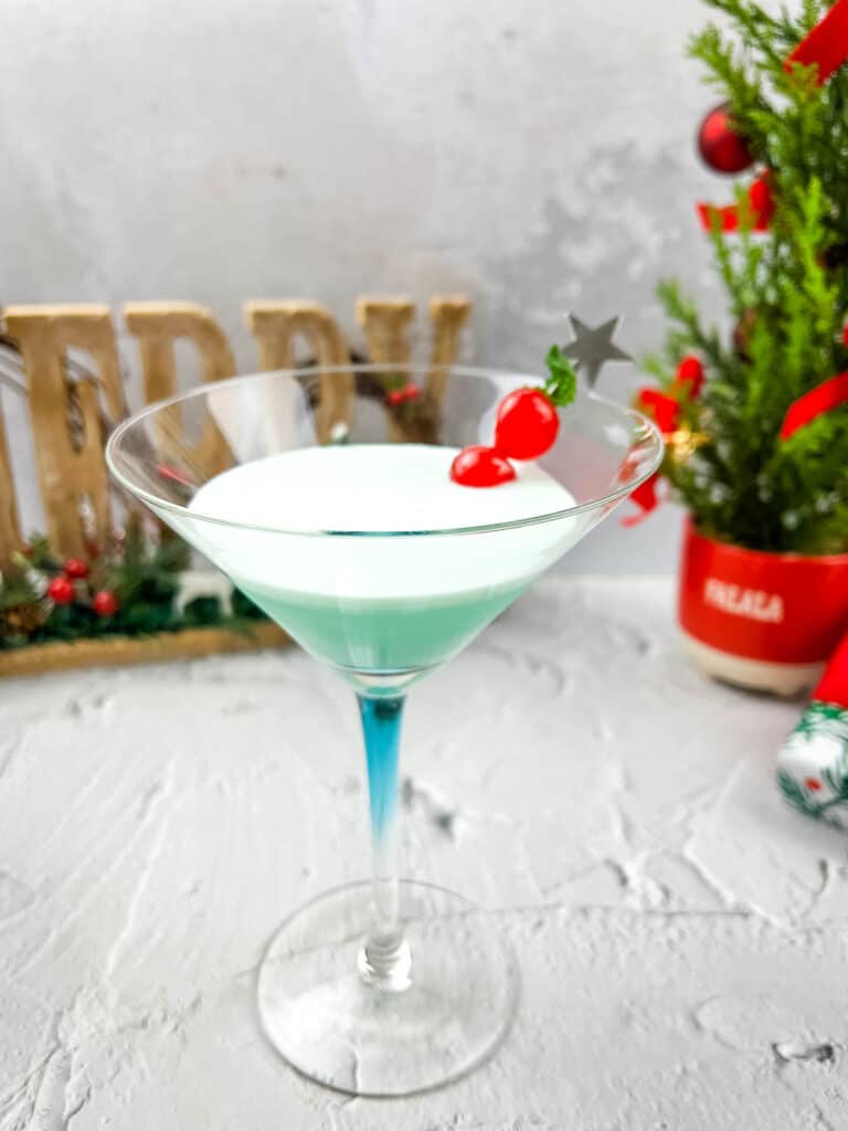 A martini in a glass with a christmas tree in the background.