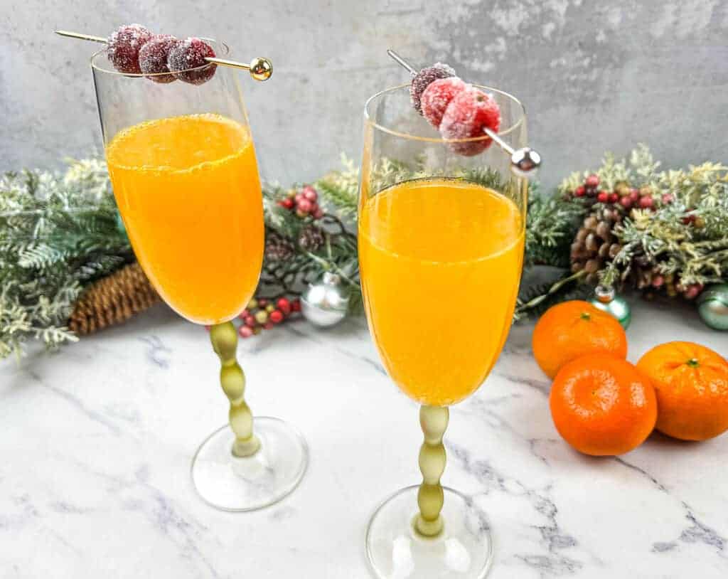 Two glasses of christmas mismosa with oranges and cranberries.
