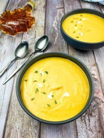 Two bowls of butternut squash and sweet potato soup on a wooden table.