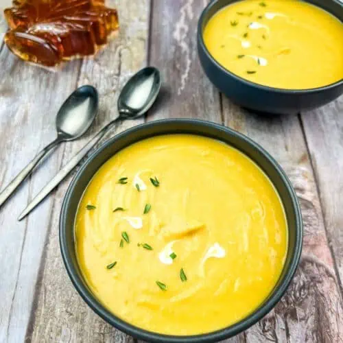 Two bowls of butternut squash and sweet potato soup on a wooden table.