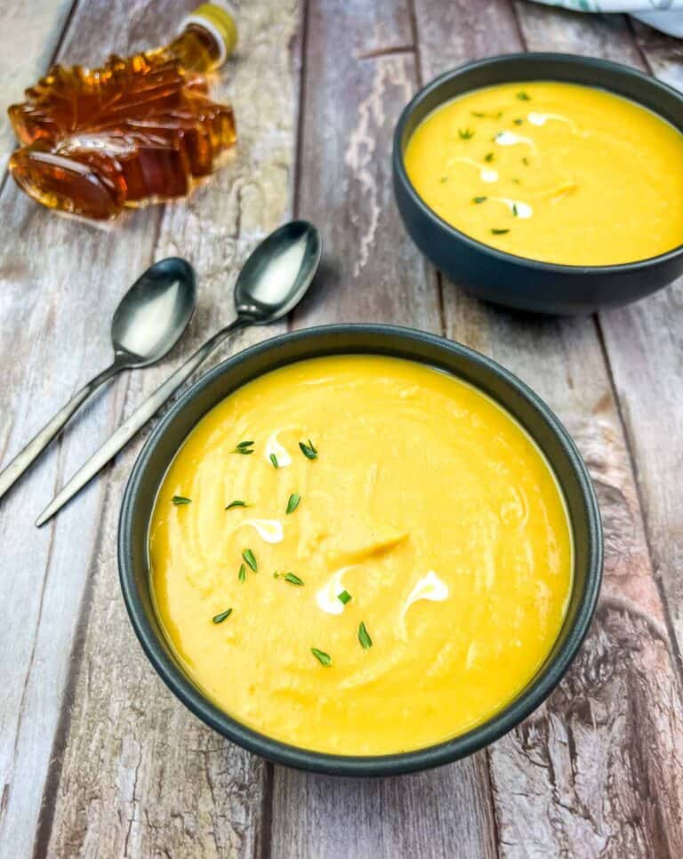 Two bowls of butternut squash and sweet potato soup on a wooden table.