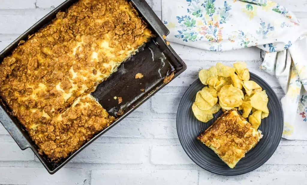 A piece of Cubano Sandwich Casserole in a pan with chips next to it.