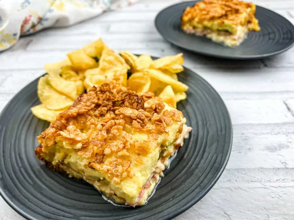 A piece of Cuban Sandwich casserole on a plate with potato chips.